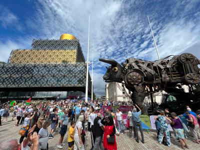 A large amount of people gather around the large figure of a bull.