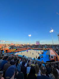 Large crowd watch beach volleyball on a sand pitch.