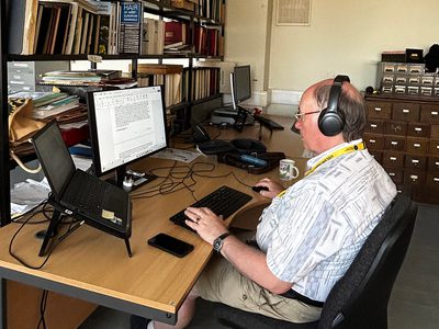 A volunteer wearing headphones working on a computer at desk.