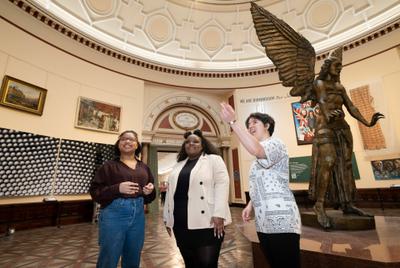 Three young women stand in the gallery, smiling as they look around them.