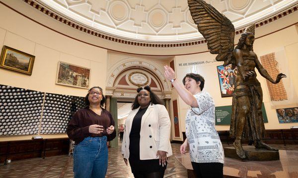 Three young women stand in the gallery, smiling as they look around them.