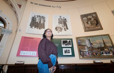 A young woman is pictured standing in the gallery with art works behind her.