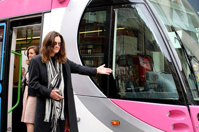 Ozzy Osbourne posing in front of the Midland Metro tram. His left hand is extending out towards the tram.
