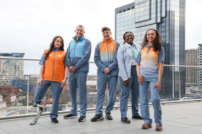 A group of five people wearing Commonwealth Games uniform, standing outside in front of a high-rise building.