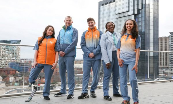 A group of five people wearing Commonwealth Games uniform, standing outside in front of a high-rise building.
