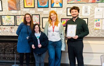 A group of people standing proudly in front of artwork created by Citizens of Midland Mencap.