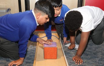 Three children closely examine a block on a track, engaged in a hands-on learning activity.
