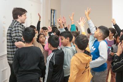 A group of children with a member of staff, many of the children standing with their hand in the air.