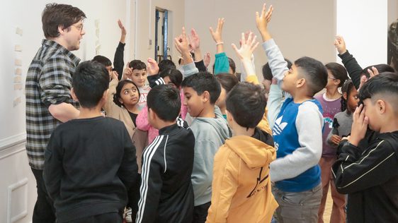 A group of children with a member of staff, many of the children standing with their hand in the air.