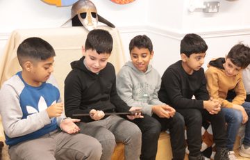 A row of children sitting on a bench, one is holding a replica Anglo-Saxon sword.