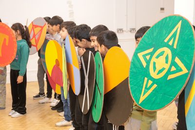A row of smiling children holding cardboard shields.