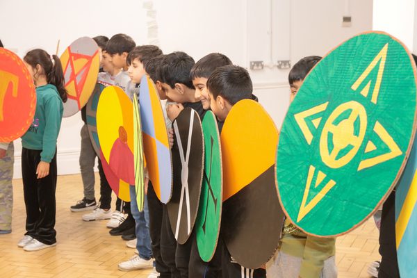 A row of smiling children holding cardboard shields.
