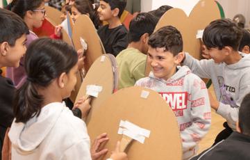 A group of smiling children holding cardboard shields pretending to fight and have a battle.