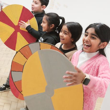 A row of smiling children holding cardboard shields.