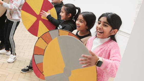 A row of smiling children holding cardboard shields.