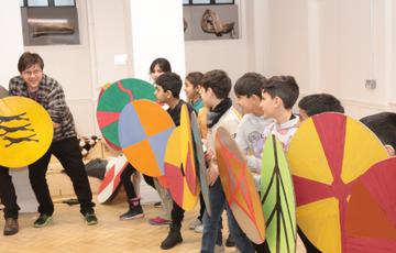 A row of smiling children holding cardboard shields.