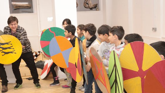 A row of smiling children holding cardboard shields.