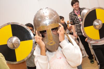 A child wearing a replica Staffordshire Hoard helmet with children behind holding replica yellow and black shields.