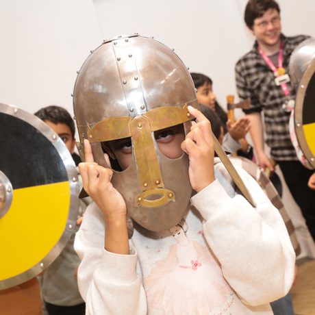 A child wearing a replica Staffordshire Hoard helmet with children behind holding replica yellow and black shields.
