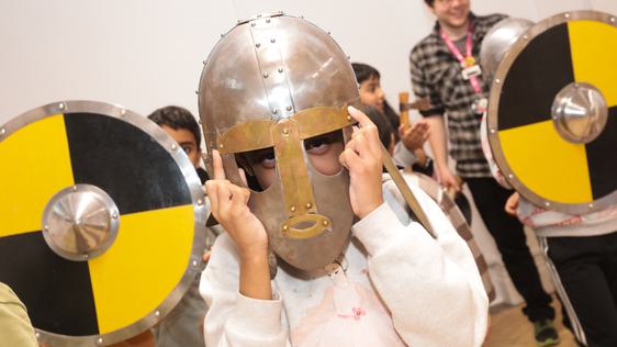 A child wearing a replica Staffordshire Hoard helmet with children behind holding replica yellow and black shields.