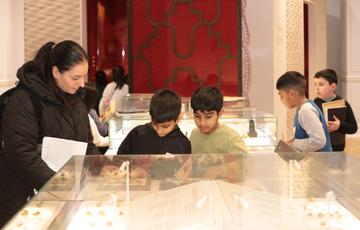 A group of children and adult looking at small gold objects on display in a perspex case.