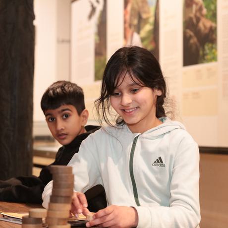 Two children sitting at a table with counters and worksheets in front of them.