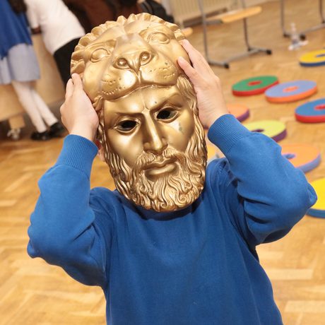 A child wearing a Greek gold coloured mask.