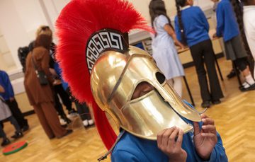A child wearing a Greek gold coloured helmet with red crest.