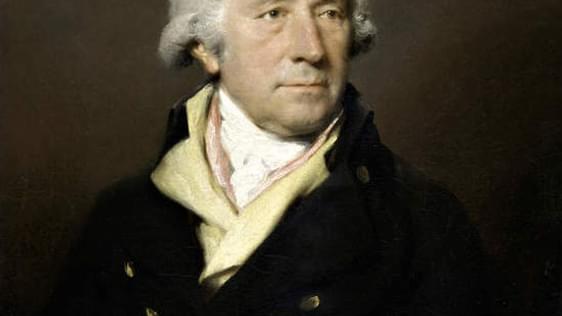 An old portrait painting of Matthew Boulton. He looks very proud, and it looking slightly to the right of the painter. His face is lit, but the rest of the painting is very dark.
