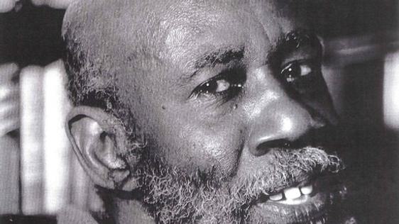 A black man looks at the camera. The portrait is closely cropped