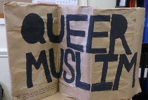 Brown paper banner with the words "Queer Muslim" painted on it