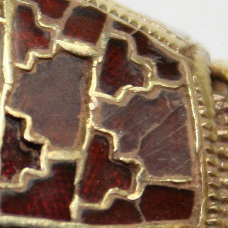 A close up photograph of a gold, garnet and glass object. The colours are gold and red.