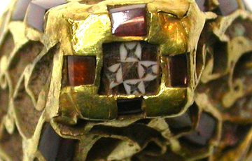 A close up photograph of a gold, and glass pyramid. It is very intricate, and the centre feature is a complex geometric design of red and white squares.