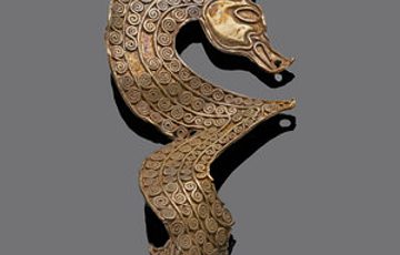 A gold object on a grey background. Gold object described as a Horse mount