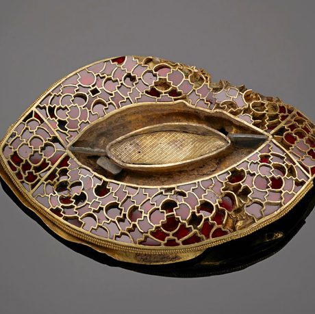 An eye-shaped gold and garnet mount. It's very intricate and delicate. It's on a grey background.