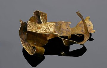 A gold object on a grey background. Gold object described as a Gold Folded Cross