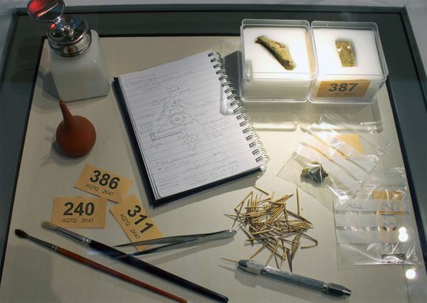 a photo of conservator tools on a table. Tools include a notebook, paint brushes, tweezers, pins, and number markers