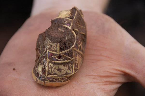a close up of an artefact being held in someone's palm. The object is gold in colour and is highly decorated.