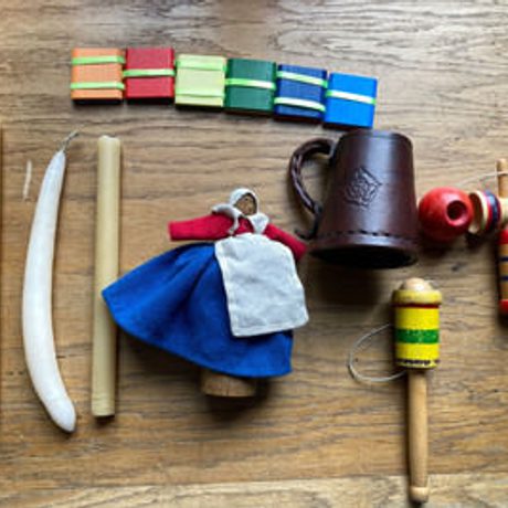 A series of items on a wooden table. Includes a leather cup, some wooden toys and some candles