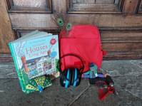A book, a red rucksack, headphones and a small soft toy resting against a wooden door