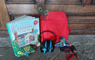 A book, a red rucksack, headphones and a small soft toy resting against a wooden door
