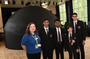 A Learning Officer and secondary school pupils standing in a school hall in front of the inflated planetarium dome.