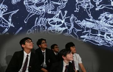 A group of secondary-age school children sitting in a mobile planetarium looking up at constellations in the sky.