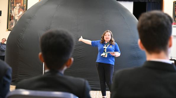 Back of students heads looking at a learning Officer who is standing in front of a mobile planetarium.