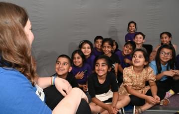 A member of the Learning Team in front of a group of smiling children who are all sat in a mobile Planetarium dome.