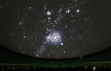 Stars and galaxies projected onto a Planetarium ceiling with seats underneath.