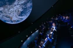 A group of school children sitting in a planetarium with the earth above them