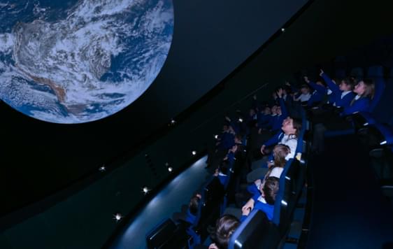 A group of school children sitting in a planetarium with the earth above them
