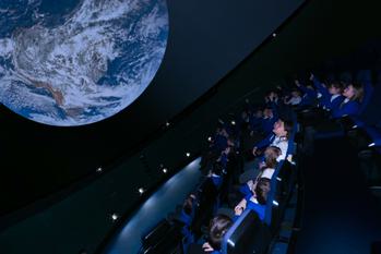 A group of schoolchildren watch a film on a planetarium screen