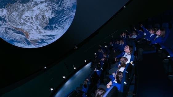 A group of schoolchildren watch a film on a planetarium screen